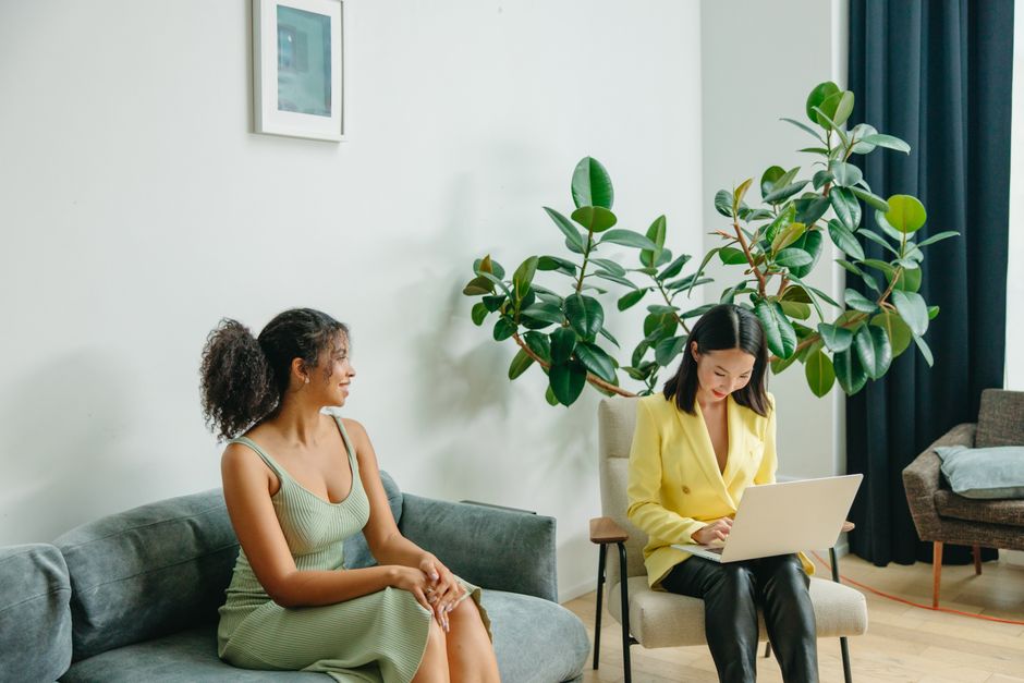 Two women engaged in a friendly consultation on a sofa in a modern, green-decor room.